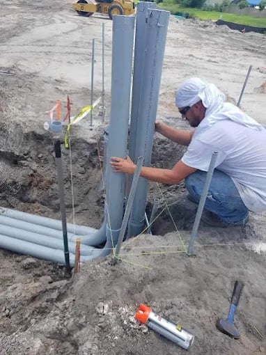 Construction worker installing large PVC pipes in excavation site with heavy equipment visible
