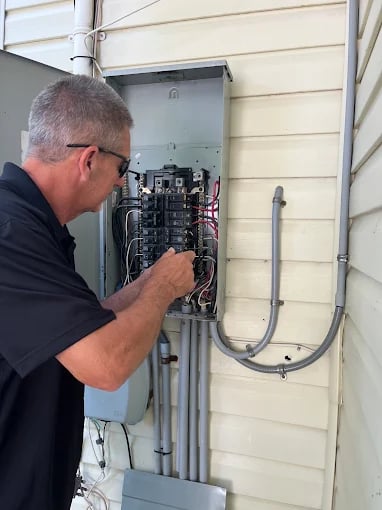Electrician inspecting residential electrical panel on house exterior wall
